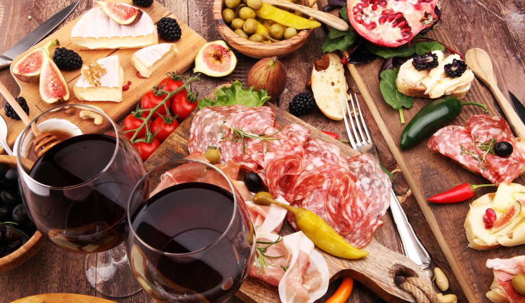 Mediterrane Abendplatte mit Krker Schinken, Schafskäse, Oliven und Wein vor einem stimmungsvollen Hintergrund.