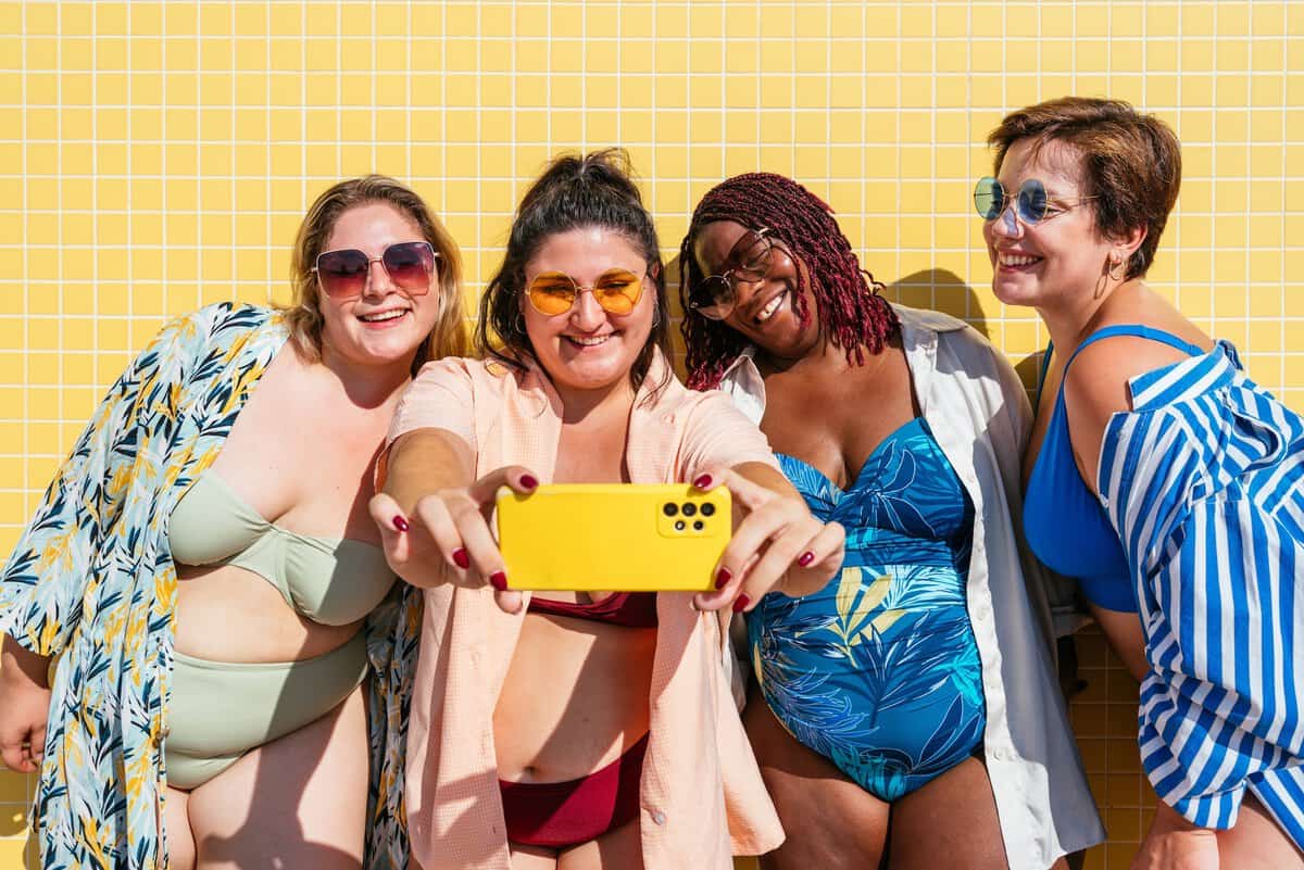 Vier lachende junge Frauen im sommerlichen Outfit machen gemeinsam ein Selfie