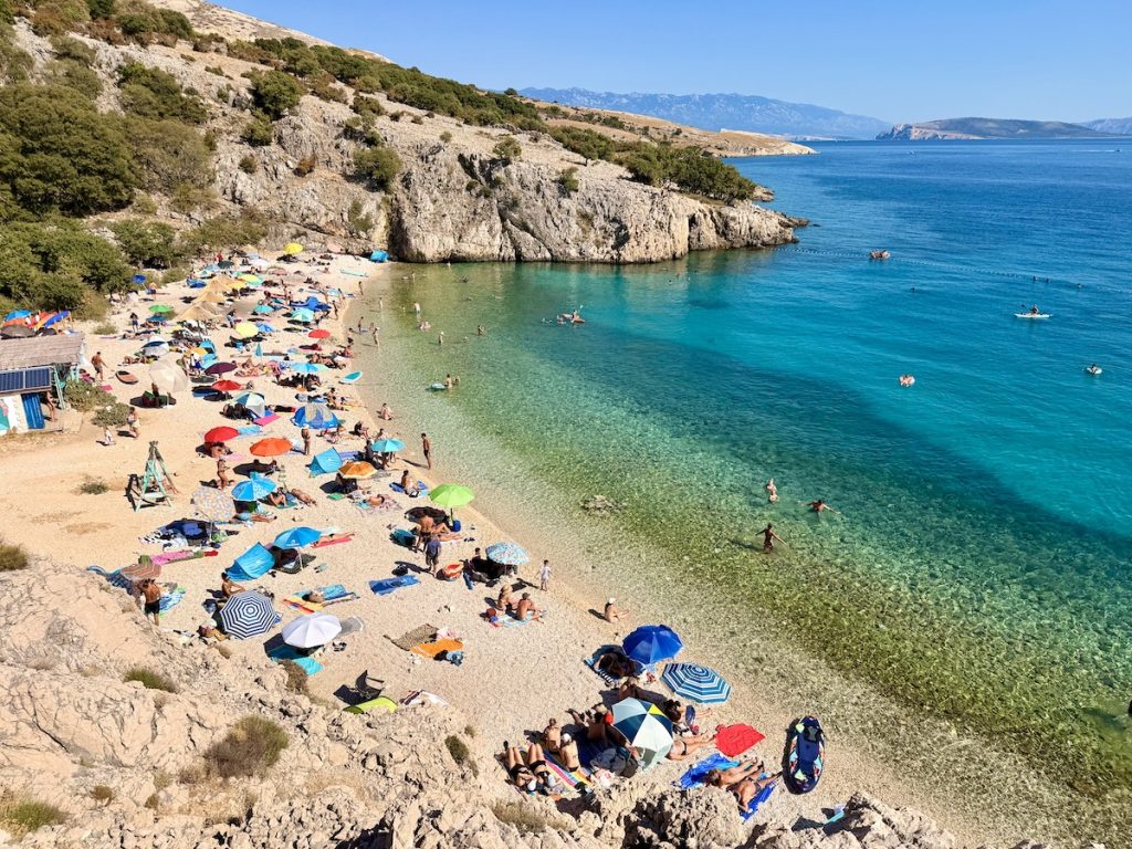 Badebucht Zala auf der Insel Krk mit Beach Bar, türkisblauem Meer durch kühle Süßwasserquellen und Badegästen.