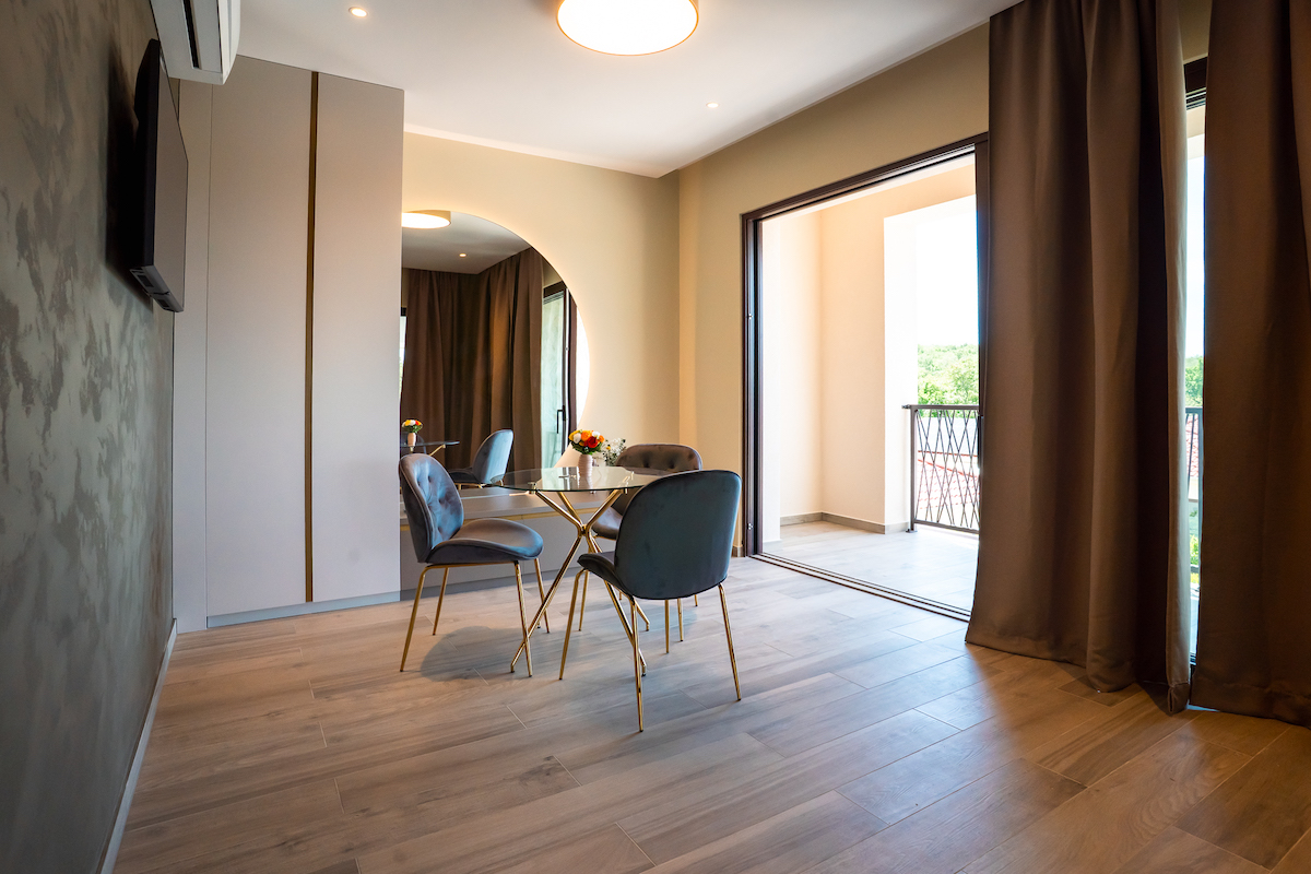 Heller Essbereich mit Glastisch, eleganten Samtstühlen und direktem Zugang durch große Schiebetüren auf den privaten Balkon im 48 m² großen Studio-Apartment des VSG Resorts.