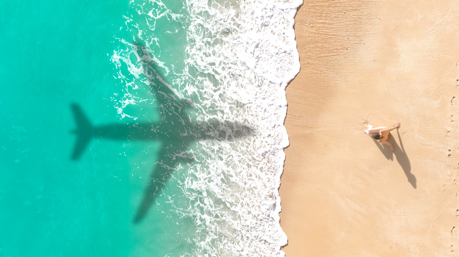Eine Frau am Strand der Insel Krk blickt nach oben, während ein Flugzeug im Landeanflug über sie hinwegfliegt und einen Schatten auf den Sand wirft.