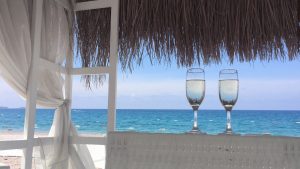 Zwei Gläser am sonnigen Strand mit Meerblick. Text: "#URLAUBAUFKRK" und Buttons für Instagram, Facebook und WhatsApp.