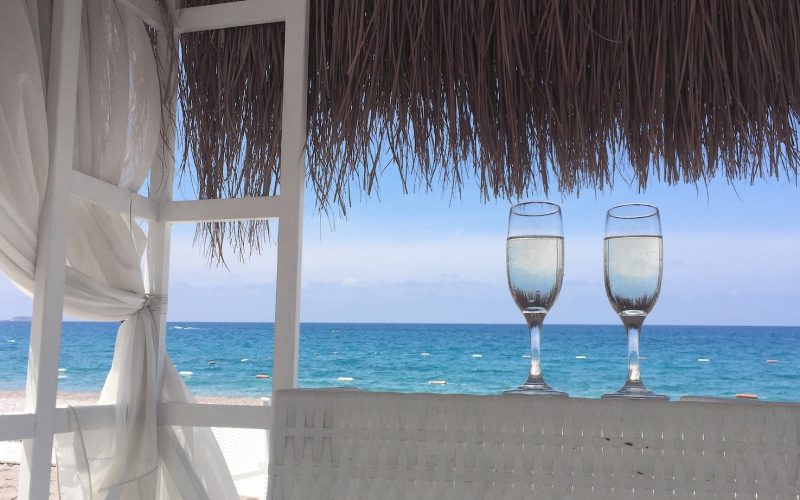 Zwei Gläser am sonnigen Strand mit Meerblick. Text: "#URLAUBAUFKRK" und Buttons für Instagram, Facebook und WhatsApp.