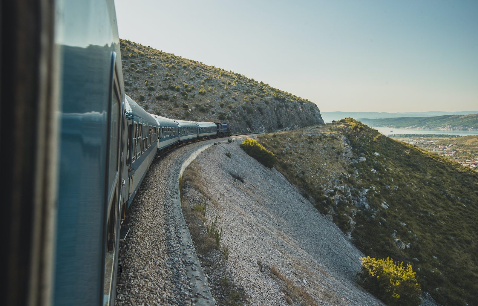 Ein Personenzug fährt entlang der Adriaküste auf der Strecke nach Rijeka mit weitem Panoramablick über das blaue Meer.