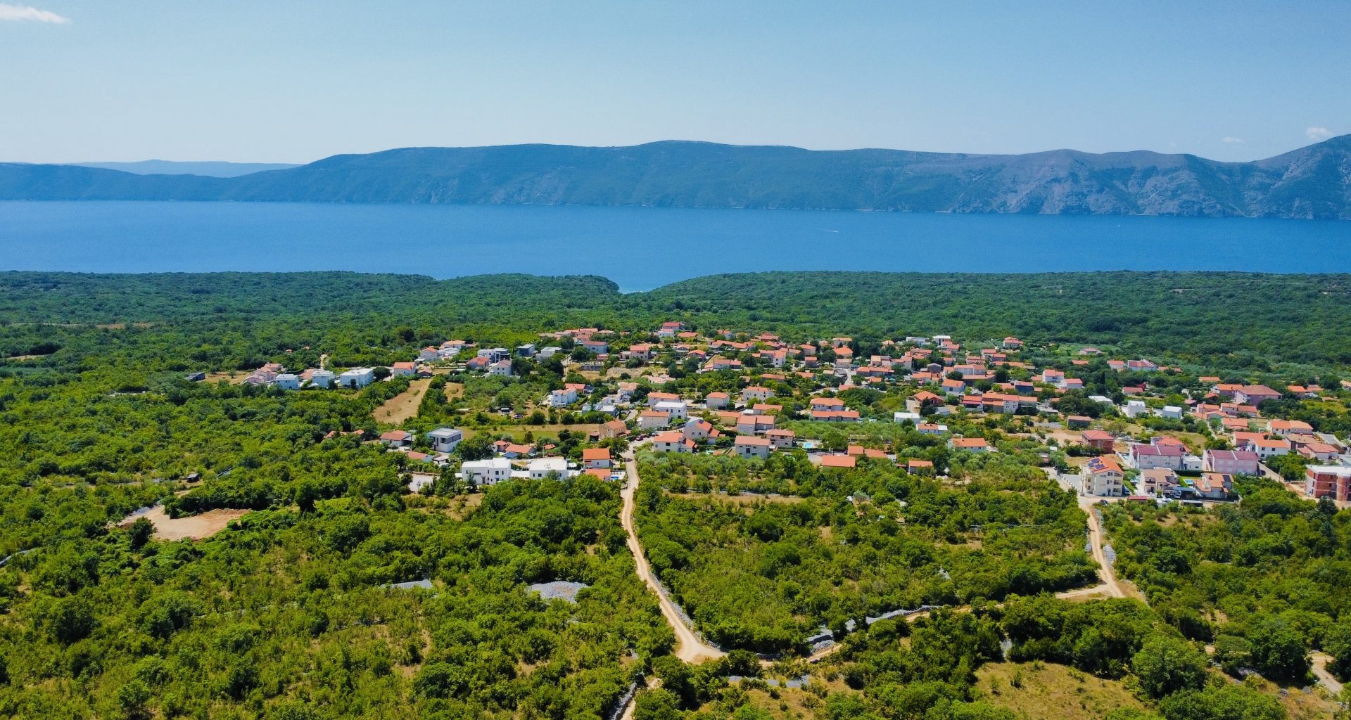 Drohnenaufnahme Dorf Linardici auf der Insel Krk umgeben von Wald mit Meerblick.