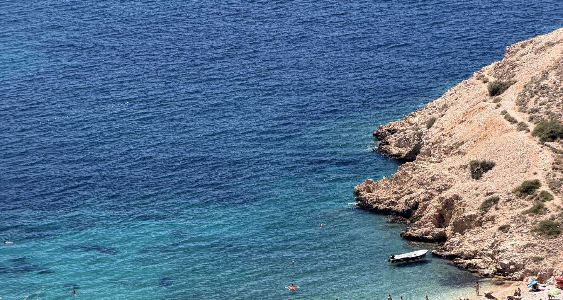 Blick von oben auf den Oprna Beach bei Stara Baška auf der Insel Krk mit Badegästen und Booten im türkisen Wasser.