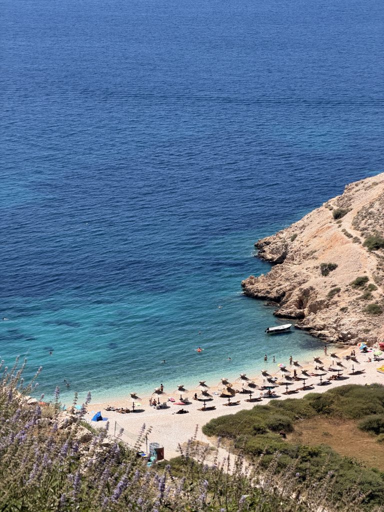 Blick von oben auf den Oprna Beach bei Stara Baška auf der Insel Krk mit Badegästen und Booten im türkisen Wasser.