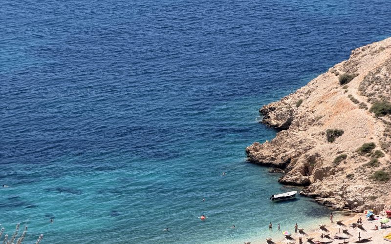 Blick von oben auf den Oprna Beach bei Stara Baška auf der Insel Krk mit Badegästen und Booten im türkisen Wasser.