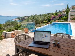 Ein Tablet zeigt einen interaktiven Rendite-Rechner für Ferienimmobilien, im Hintergrund eine luxuriöse Villa mit Pool auf der Insel Krk in Kroatien.