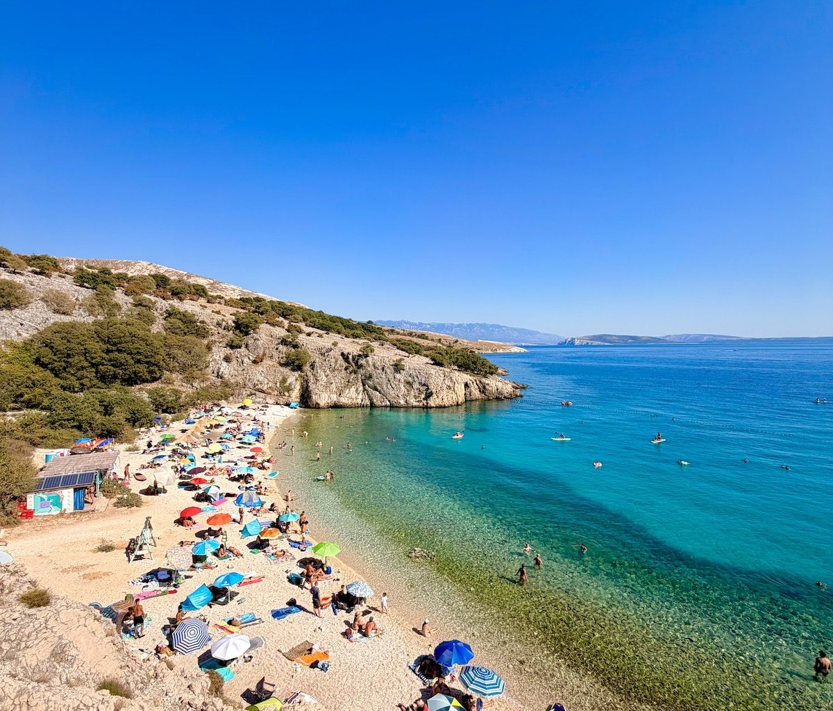 Badebucht Zala auf der Insel Krk mit Beach Bar, türkisblauem Meer durch kühle Süßwasserquellen und Badegästen.