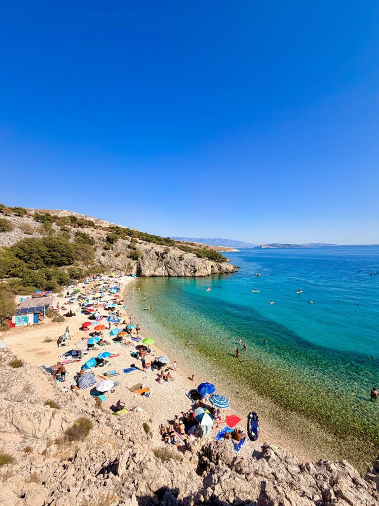 Badebucht Zala auf der Insel Krk mit Beach Bar, türkisblauem Meer durch kühle Süßwasserquellen und Badegästen.
