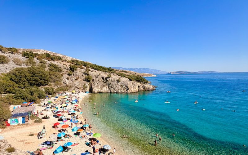 Badebucht Zala auf der Insel Krk mit Beach Bar, türkisblauem Meer durch kühle Süßwasserquellen und Badegästen.