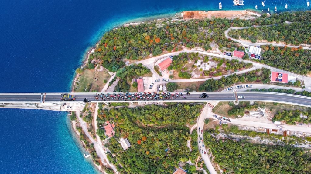 Luftaufnahme der Krk-Brücke während des CRO Race. Ein großes Feld an Radrennfahrern und Begleitfahrzeugen überquert die komplette Fahrbahn.
