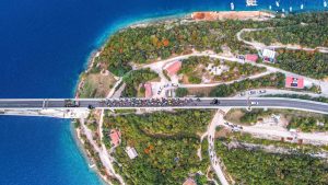 Luftaufnahme der Krk-Brücke während des CRO Race. Ein großes Feld an Radrennfahrern und Begleitfahrzeugen überquert die komplette Fahrbahn.