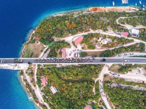 Luftaufnahme der Krk-Brücke während des CRO Race. Ein großes Feld an Radrennfahrern und Begleitfahrzeugen überquert die komplette Fahrbahn.