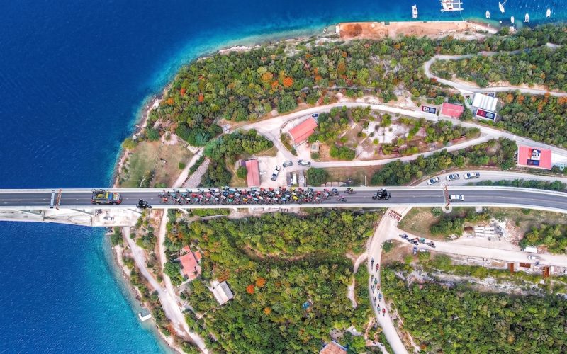 Luftaufnahme der Krk-Brücke während des CRO Race. Ein großes Feld an Radrennfahrern und Begleitfahrzeugen überquert die komplette Fahrbahn.